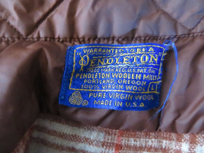 May include: Close-up of a blue Pendleton label with gold lettering, stitched onto a brown quilted fabric. The label reads "Pendleton Woolen Mills, Portland, Oregon, 100% Virgin Wool, Made in U.S.A."