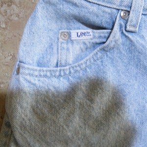 May include: Light blue denim jeans with a faded appearance and a Lee brand label on the front pocket.