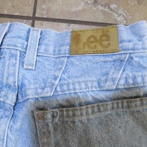 May include: Light blue denim jeans with a brown leather patch that says "Lee" on the back waistband.