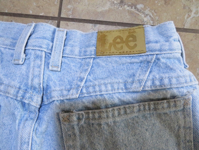 May include: Light blue denim jeans with a brown leather patch that says "Lee" on the back waistband.
