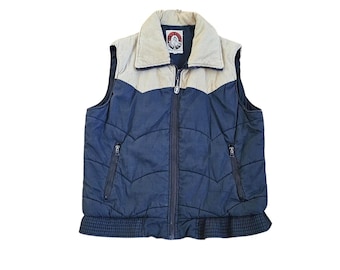Op de afbeelding: Een marineblauw gewatteerd vest met een beige corduroy schouderstuk en kraag. Het kledingstuk heeft een ritssluiting aan de voorzijde, twee zijzakken met rits en een geribbelde zoom. Een rond "RED KAP"-logo is zichtbaar in de binnenhals.