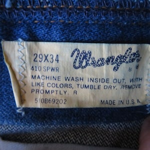 May include: A white Wrangler jeans care label with black text. The label reads "29X34", "410 SPWR", "MACHINE WASH INSIDE OUT, WITH LIKE COLORS, TUMBLE DRY, REMOVE PROMPTLY. R", "510B69202", and "MADE IN U.S.A."