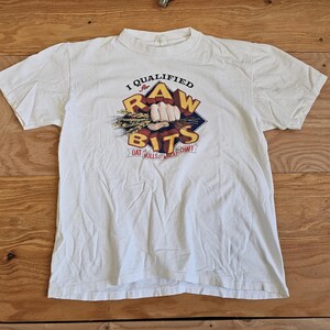 May include: White t-shirt with a graphic of a hand holding wheat stalks and the text "I Qualified for the Raw Bits Oat Hulls & Wheat Chaff"