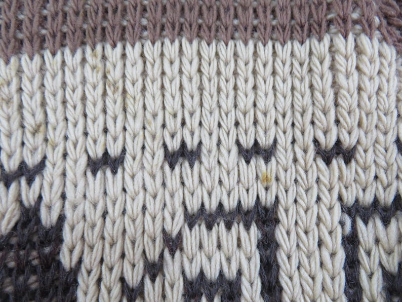 Puede incluir: Primer plano de una tela de punto con un patr&oacute;n texturizado. El dise&ntilde;o presenta bandas alternas de beige claro, gris oscuro y marr&oacute;n. Las puntadas de punto crean un efecto acanalado vertical, con un patr&oacute;n geom&eacute;trico en el centro.