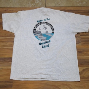 May include: A light gray t-shirt with a circular graphic on the back. The graphic includes text that reads "Home of the WJC Section Conclave 1994" and "On This First Step National Chief". The design features a deer and a lake.