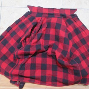 May include: A long-sleeved button-down shirt featuring a bold red and black buffalo plaid pattern. The garment is displayed with the collar visible at the top and the front placket showing a series of dark buttons along the right side edge.