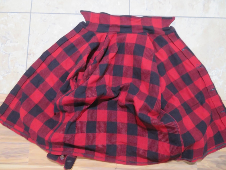 May include: A long-sleeved button-down shirt featuring a bold red and black buffalo plaid pattern. The garment is displayed with the collar visible at the top and the front placket showing a series of dark buttons along the right side edge.