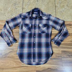 Peut inclure: Une chemise à carreaux à manches longues dans les tons de bleu, de rouge et de blanc. La chemise comporte deux poches de poitrine avec des rabats pointus et des fermetures à boutons-pression nacrés. Elle a un style western classique.