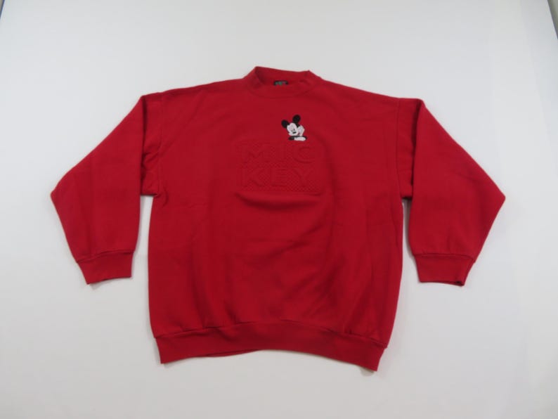 Puede incluir: Una sudadera roja con cuello alto y mangas largas. La sudadera presenta un dise&ntilde;o bordado de Mickey Mouse en la parte superior izquierda del pecho y las palabras "Mickey" en relieve debajo. Los pu&ntilde;os y el dobladillo son acanalados.