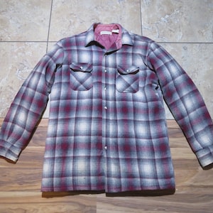 May include: A button-down, long-sleeve shirt with a plaid pattern in shades of burgundy, white, and gray. The shirt has two chest pockets and a quilted, pink interior lining. The shirt is made of a thick, warm material.
