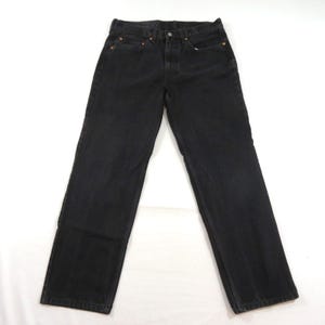 Könnte beinhalten: Eine schwarze Jeans aus Denim mit klassischem Fünf-Taschen-Design, Knopfleiste und kupferfarbenen Metallnieten an den Taschenecken. Die Hose hat einen geradlinigen Schnitt mit sichtbaren Nähten entlang der Beine und einen Hosenbund.