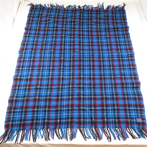 May include: A rectangular throw blanket featuring a vibrant blue, black, and red plaid tartan pattern. The blanket has a soft, textured appearance and is finished with long, loose fringe detailing along both the top and bottom edges.