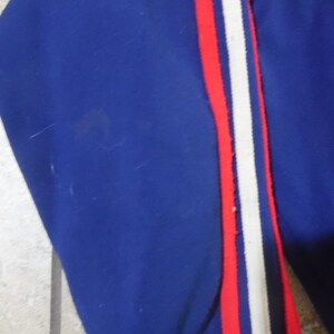 May include: A royal blue garment featuring a vertical side stripe detail. The stripe consists of a central white band flanked by two thin red lines. The fabric appears to be a smooth, solid-colored material with a consistent texture throughout the piece.