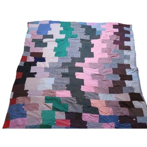 May include: A rectangular patchwork quilt constructed from various fabric squares in shades of pink, green, blue, brown, gray, and red. The textile features a staggered, interlocking pattern with small, light pink fabric knots at the corners.