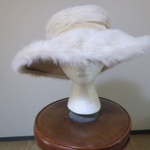 May include: A white fur hat with a wide brim. The hat is sitting on a brown stool.