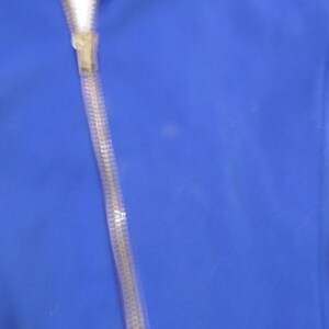 May include: A vibrant royal blue fabric surface featuring a vertical, semi-transparent, textured plastic zipper track running down the center. The zipper pull is a clear, molded plastic component attached to the top of the flexible, ribbed track.