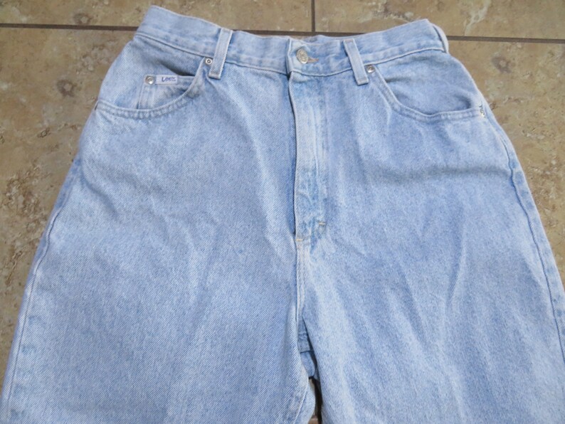 May include: Light blue denim jeans with a high waist and a classic five-pocket style. The jeans have a faded look and a relaxed fit.
