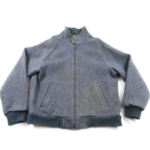Puede incluir: Una chaqueta tipo bomber gris de mezcla de lana con cremallera frontal completa, cuello alzado con cierre de botón a presión, dos bolsillos delanteros inclinados y puños y dobladillo de punto acanalado en color gris oscuro.