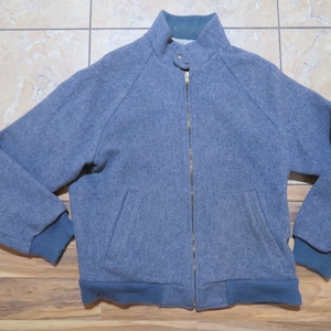 May include: A grey jacket with a full zip, a stand-up collar, and two front pockets. The jacket has teal ribbed cuffs and a teal ribbed hem. The collar has a teal lining.