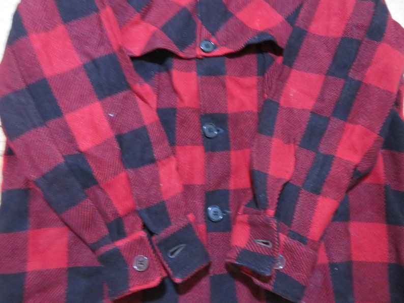 May include: A long-sleeve button-down shirt featuring a bold red and black buffalo plaid pattern. The garment includes a front button placket with dark buttons and matching buttoned cuffs at the end of each sleeve, showcasing a classic checkered design.