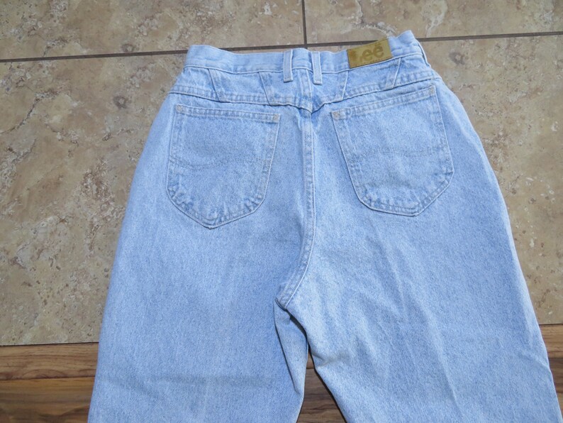 May include: A pair of light blue denim jeans with a back pocket on each side. The jeans have a brown leather patch with the word "Lee" on it.