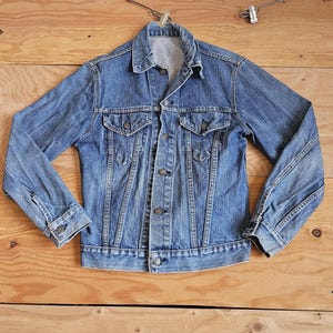 May include: A classic blue denim jacket with a button-down front, two chest pockets, and long sleeves. The jacket is made of durable denim fabric and features a collared neckline. The jacket is a timeless piece of apparel.