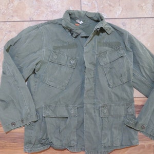 Puede incluir: Una chaqueta verde de utilidad con múltiples bolsillos y cierres de botón. La chaqueta tiene cuello y mangas largas.