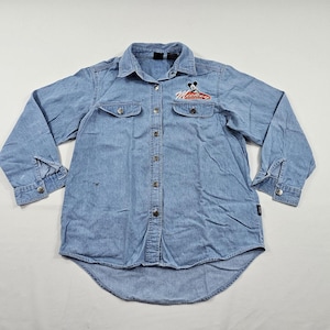 May include: A light blue denim button-down shirt featuring a pointed collar, long sleeves with buttoned cuffs, and two chest pockets. An embroidered graphic of Mickey Mouse with the red text Mickey Mouse is positioned above the left pocket.