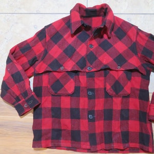 Może przedstawiać: Czerwono-czarna koszula w kratę z flaneli z kołnierzykiem, zapięciem na guziki z przodu i dwiema kieszeniami na piersi. Koszula ma długie rękawy z mankietami zapinanymi na guziki. Klasyczna koszula w stylu drwala wykonana jest z grubego, ciepłego materiału.