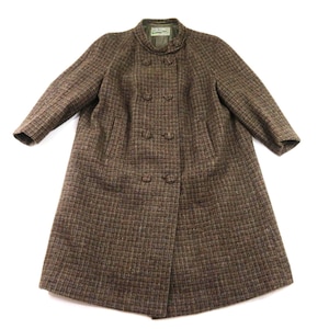 May include: A brown and dark tan tweed coat featuring a double-breasted front with five fabric-covered buttons, a high mandarin-style collar, long sleeves, and two vertical slit pockets. The coat has a textured woven pattern and a solid lining.