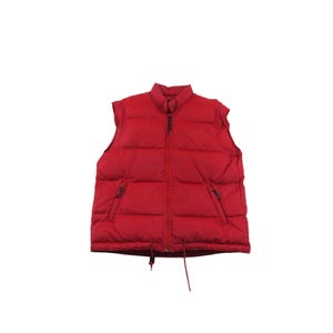 May include: A bright red puffer vest featuring a high collar, a full-length front zipper, and two side pockets with zipper closures. The garment has a quilted, horizontal-baffled design and includes a drawstring cord at the bottom hem.