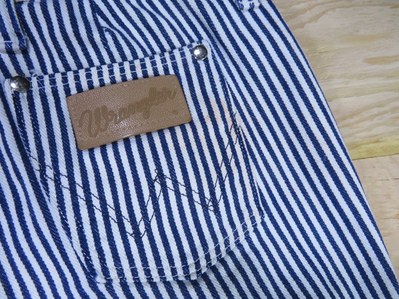 May include: Blue and white striped denim pants with a brown leather patch that says "Wrangler" on the back pocket.