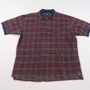 Peut inclure: Un polo à manches courtes avec un motif à carreaux dans les tons de rouge, vert et bleu marine. Le polo a un col et des poignets bleu marine, avec une patte de boutonnage à trois boutons. Le tissu est doux et confortable.