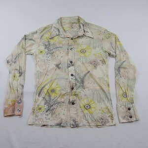 May include: A long-sleeve button-down shirt in a cream colour featuring a repeating pattern of yellow circular floral motifs and grey fern-like botanical illustrations. The shirt has a pointed collar, a front button placket, and buttoned cuffs.