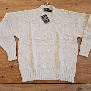 Może przedstawiać: Kremowy sweter dzianinowy z geometrycznym wzorem. Sweter ma okrągły dekolt i długie rękawy.