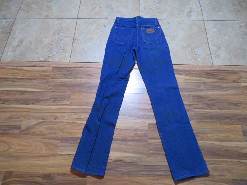 May include: A pair of blue denim jeans with a brown leather patch on the back pocket that says "Wrangler".