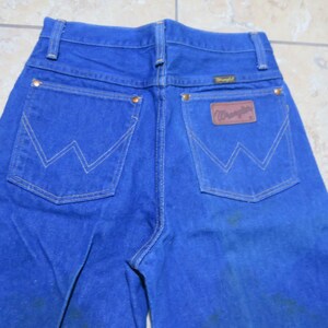 May include: A pair of blue denim jeans with a brown leather Wrangler patch on the back pocket.