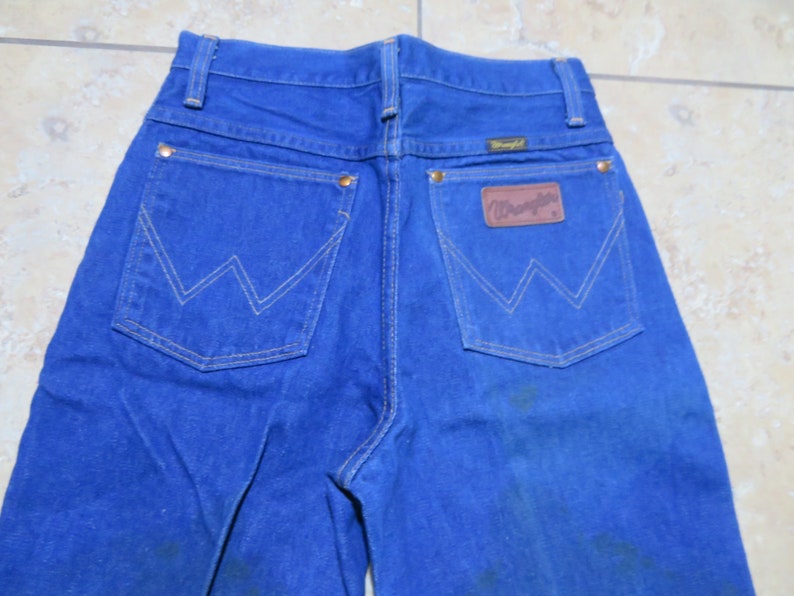 May include: A pair of blue denim jeans with a brown leather Wrangler patch on the back pocket.