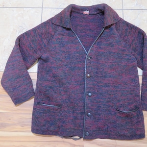 Peut inclure: Un cardigan en tricot rouge foncé et noir avec une bordure en cuir noir et une fermeture à boutons. Le cardigan a deux poches sur le devant.