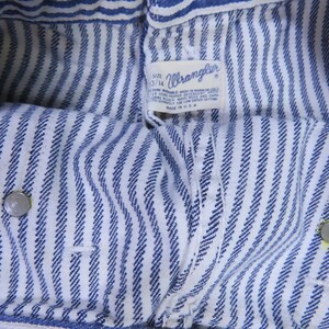 May include: Close-up of blue and white striped fabric with a Wrangler label. The label reads "Size 33/14 Machine Wash in Warm or Cold Water.  Do Not Bleach.  Wash with Like Colors.  Tumble Dry Low.  Made in U.S.A."