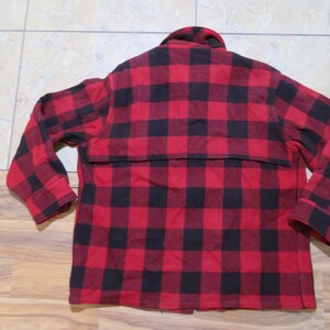 May include: A long-sleeve button-up shirt featuring a bold red and black buffalo plaid pattern. The garment includes a classic collar, a horizontal back yoke overlay, and cuffs at the end of each sleeve, showcasing a consistent checkered design.