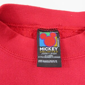 Puede incluir: Primer plano de una sudadera roja con cuello redondo. La etiqueta presenta el logotipo de Mickey Mouse y el texto "MICKEY UNLIMITED JERRY LEIGH X-LARGE EXTRA GRANDE/X GRAND". La etiqueta tambi&eacute;n dice "MADE IN U.S.A."