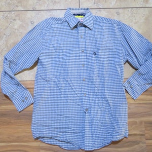 May include: A blue and white checked long-sleeved shirt with a button-down collar and cuffs. The shirt features a small logo on the chest and is made of a lightweight fabric. The shirt's design is a classic, casual style.