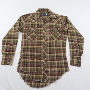 May include: A long-sleeve button-down shirt featuring a plaid pattern in shades of tan, brown, and dark red. The shirt includes a pointed collar, two chest pockets with buttoned flaps, and buttoned cuffs. The front placket has visible buttons.