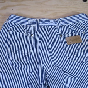 May include: Blue and white striped denim pants with a brown leather patch that says "Wrangler" on the back right pocket.