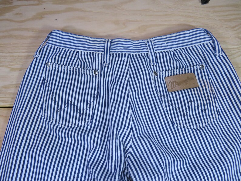 May include: Blue and white striped denim pants with a brown leather patch that says "Wrangler" on the back right pocket.