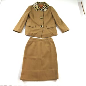 May include: A tan two-piece set consisting of a long-sleeved jacket and a matching skirt. The jacket features a leopard print collar, two front pockets, and three large buttons. The skirt is a simple, straight-cut design in the same tan colour.