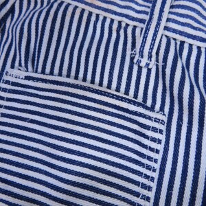 May include: Close-up of blue and white striped fabric with a pocket. The fabric has a woven texture and is sewn with white thread.