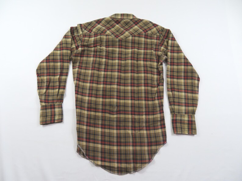 May include: A long-sleeve button-down shirt featuring a plaid pattern in shades of tan, brown, black, and dark red. The shirt has a pointed western-style back yoke, a standard collar, and long sleeves with buttoned cuffs, shown from the back view.
