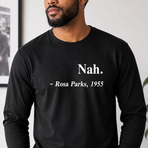 May include: Black long-sleeve shirt with the text "Nah. - Rosa Parks, 1955" in white. The shirt is worn by a person with a beard and short, dark hair. The person is wearing blue jeans.